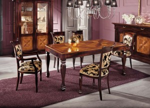 Klasični stol u kompletu sa klasičnim stolicama sa i bez rukonaslona. Ploča stola je izrađena sa interzijama. Sjedište i leđa stolica presvučene su u tkaninu. Može se naručiti u drugim bojama drva i drugim tkaninama.